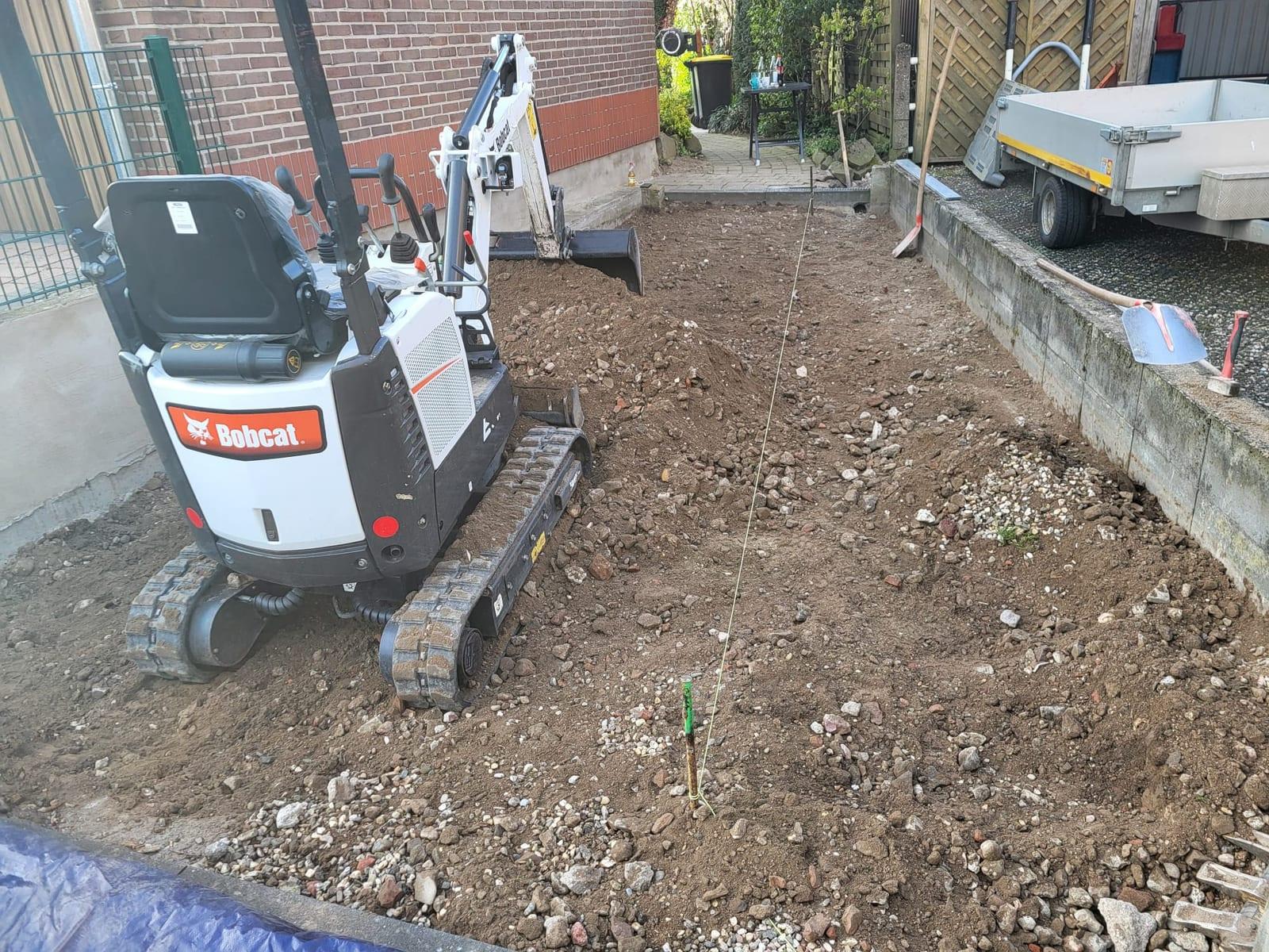 Minibagger planiert das Erdreich einer Gartenfläche und zieht sie auf ein ebenes Planum ab